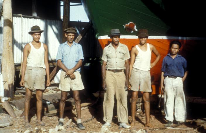 Image of boat builders standing in front of a boat. 